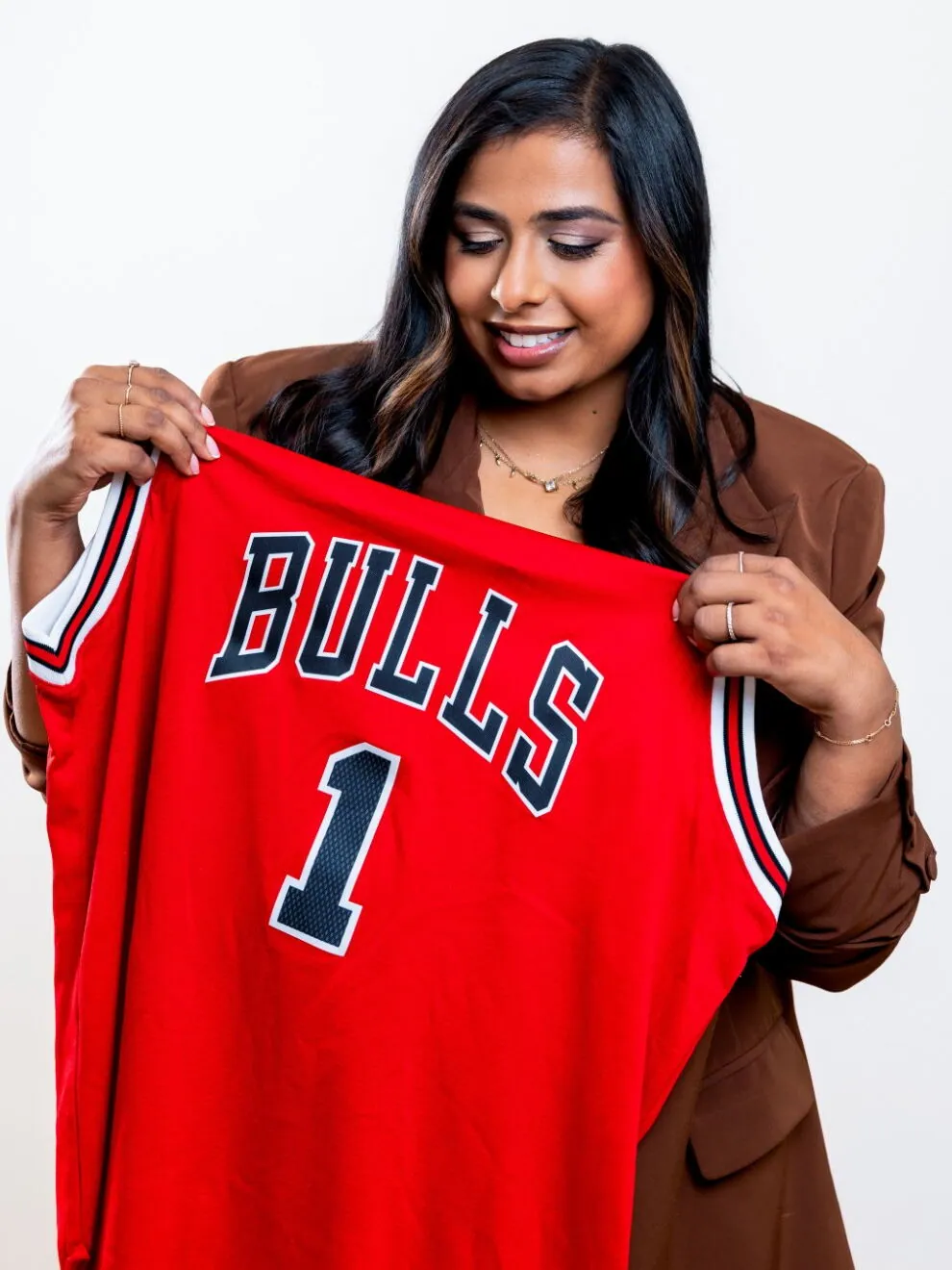Dr. Anisha Jacob smiling as she holds up a red Chicago Bulls number 1 jersey