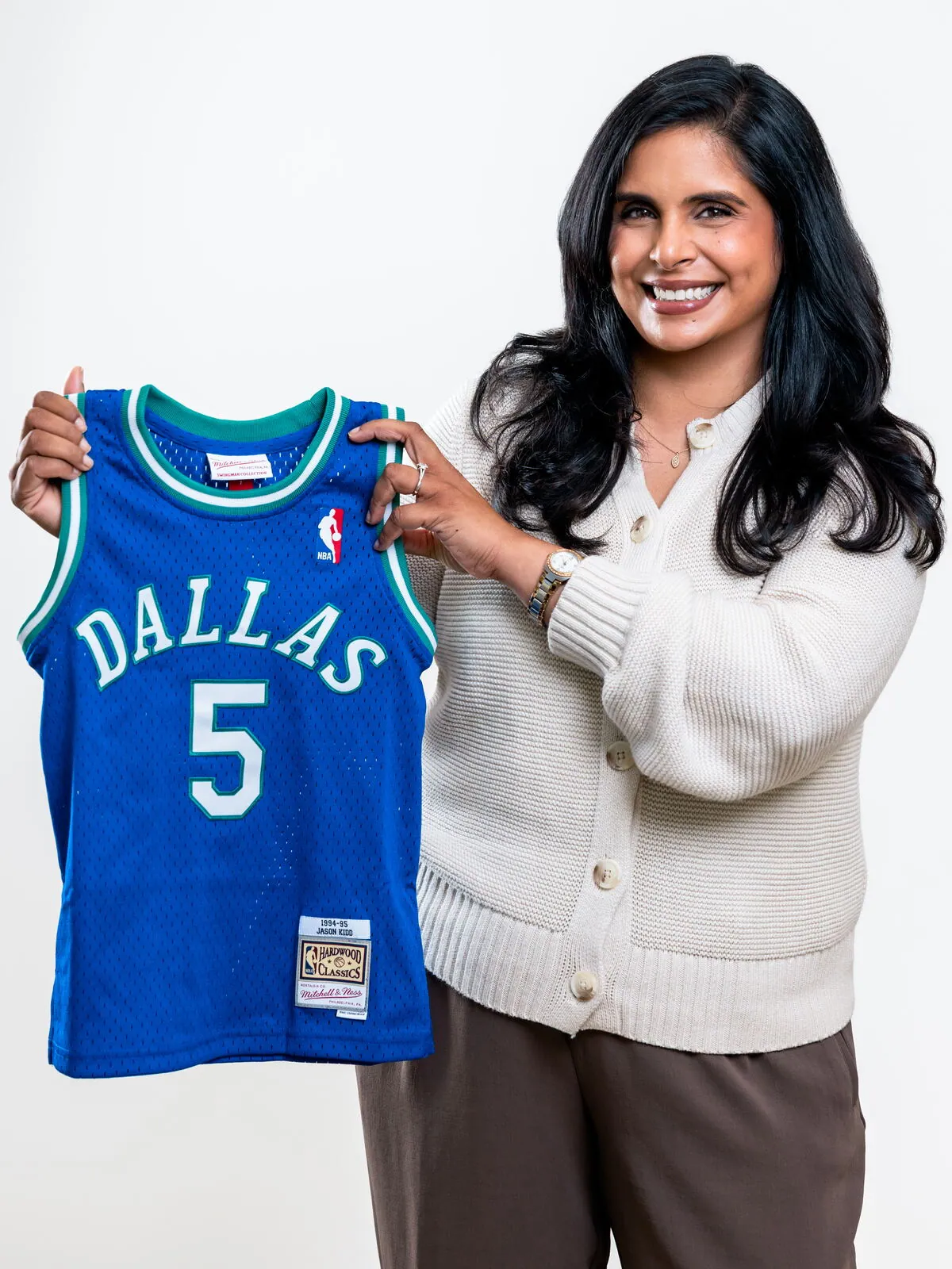 Dr. Ashley Chennankara holding up a blue Dallas Mavericks number 5 jersey