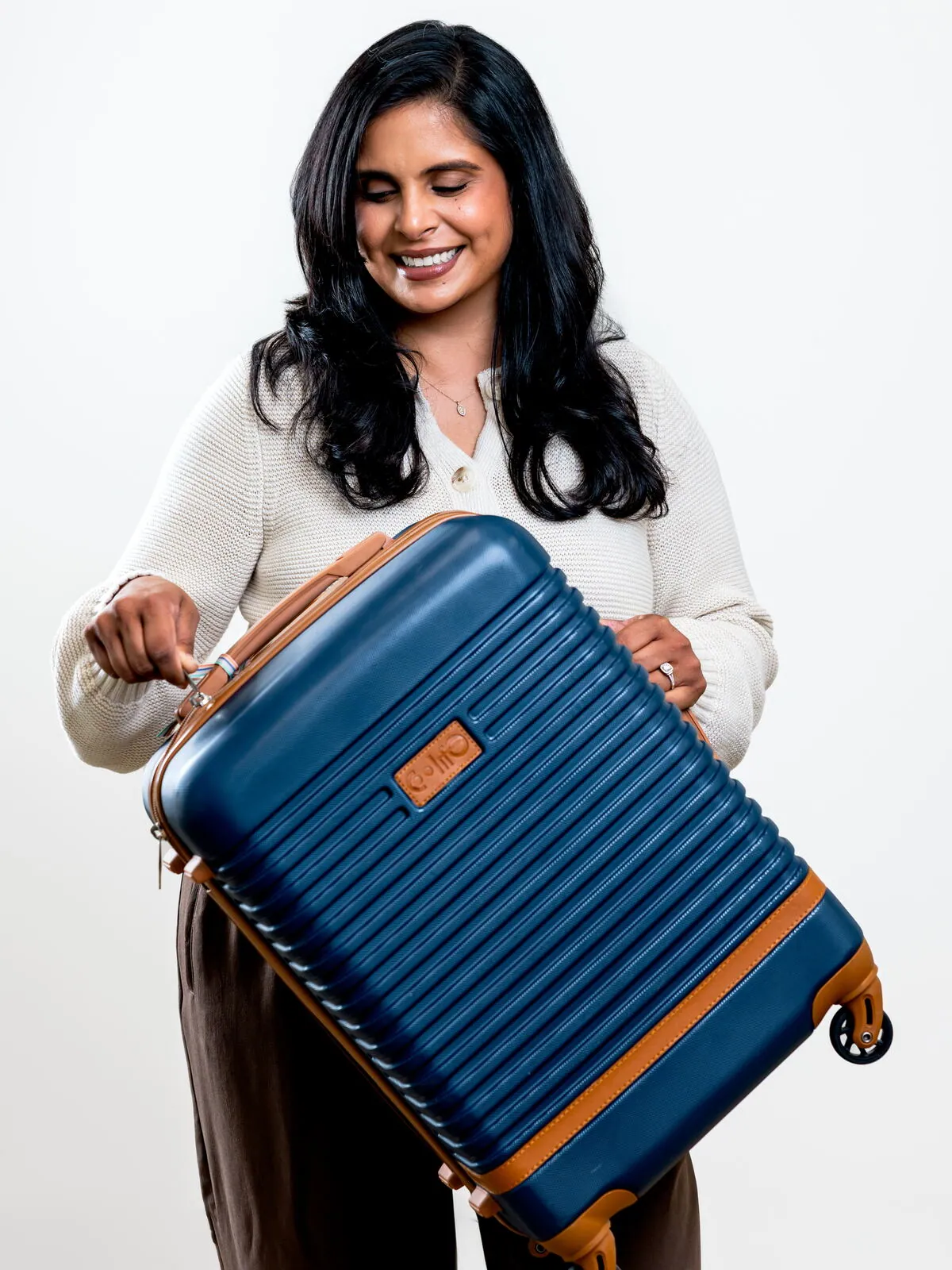 Dr. Ashley Chennankara smiling as she holds a navy carry-on suitcase