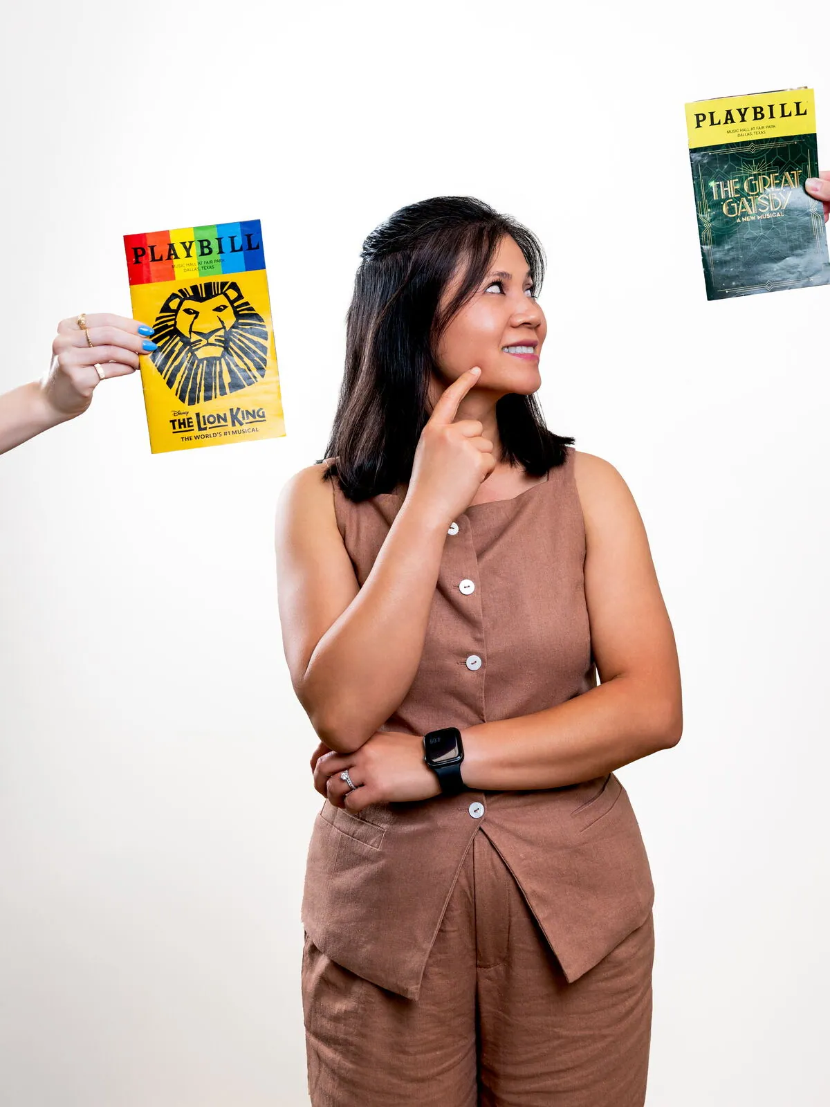 Dr. Michelle Conrad deciding between Playbills for The Lion King and The Great Gatsby
