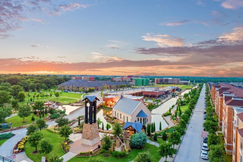 Aerial view at sunset of a canal-side town center with a clock tower in Flower Mound, TX
