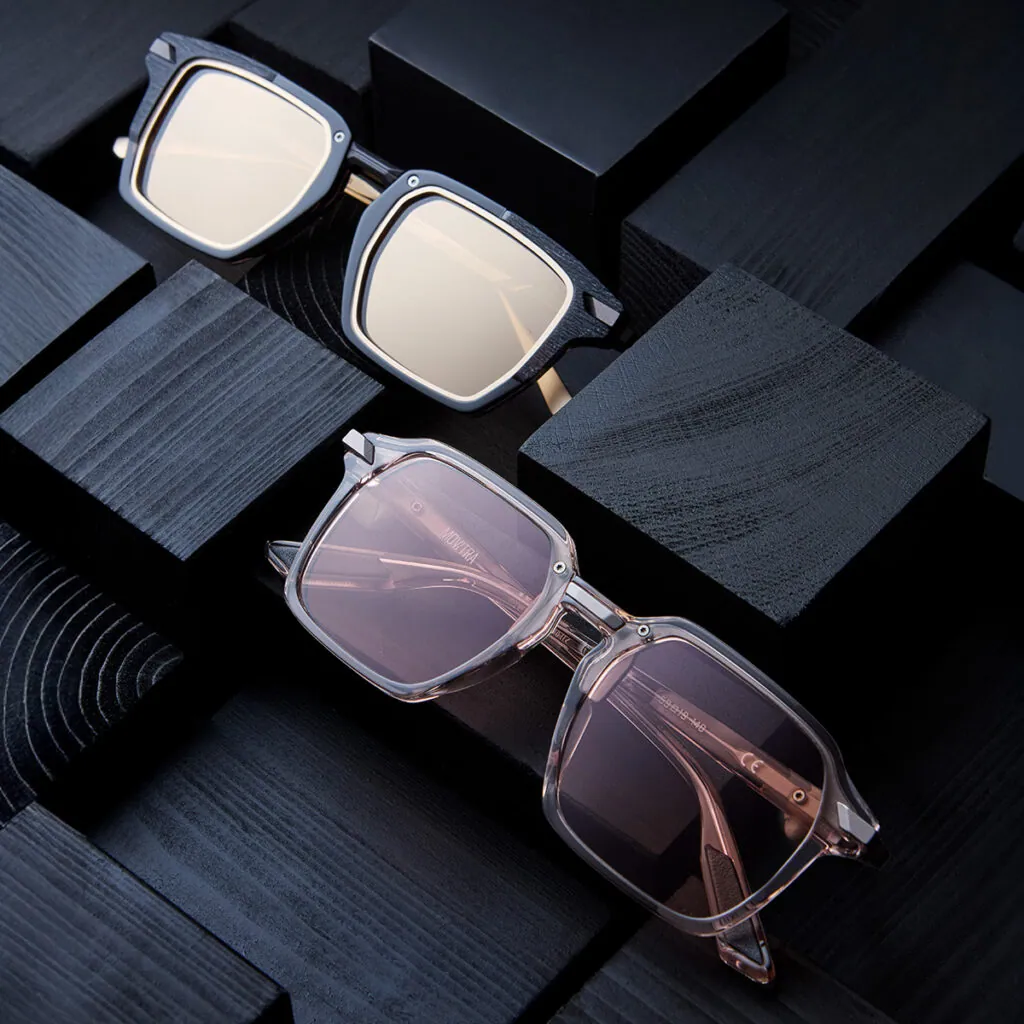 Two pairs of Movitra square frames with tinted lenses displayed on dark wood blocks