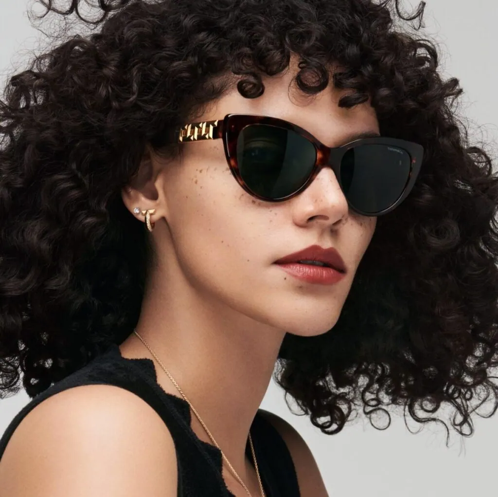 Woman with curly hair wearing Tiffany & Co. cat-eye sunglasses with gold detailing