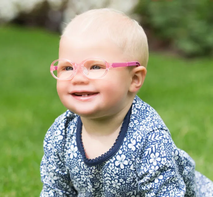 Smiling baby wearing pink flexible Tomato Glasses frames
