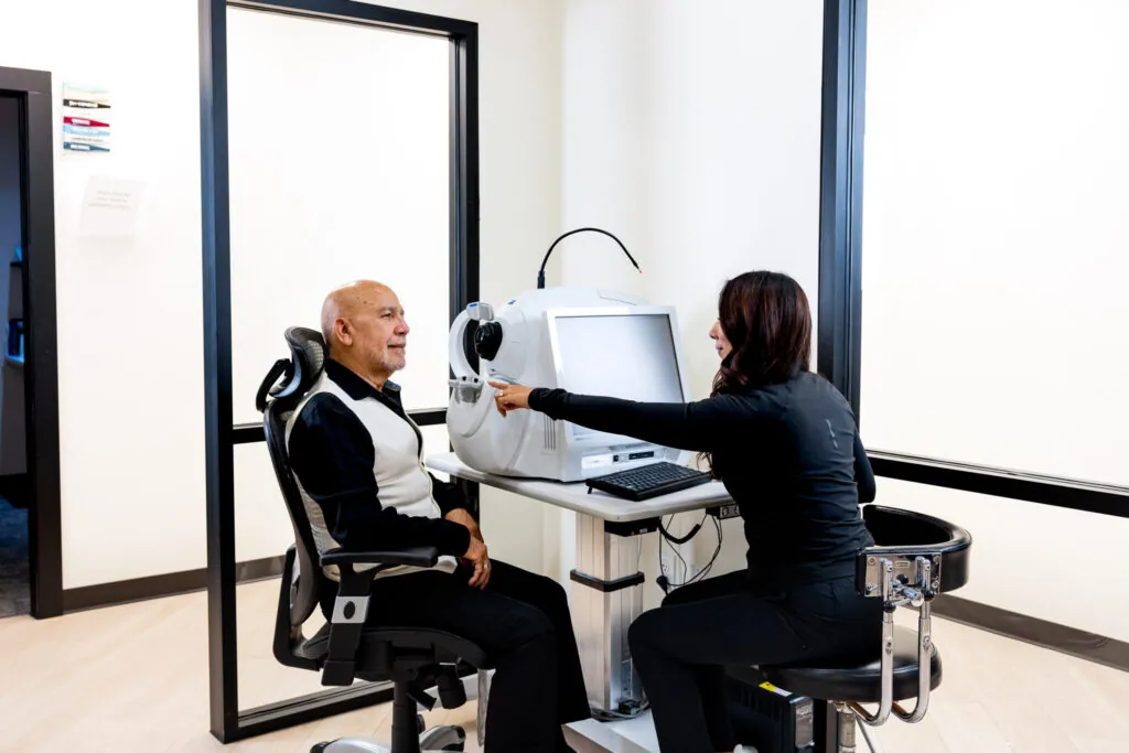 A patient seated at a diagnostic imaging instrument while a Village Vision Center team member runs the scan