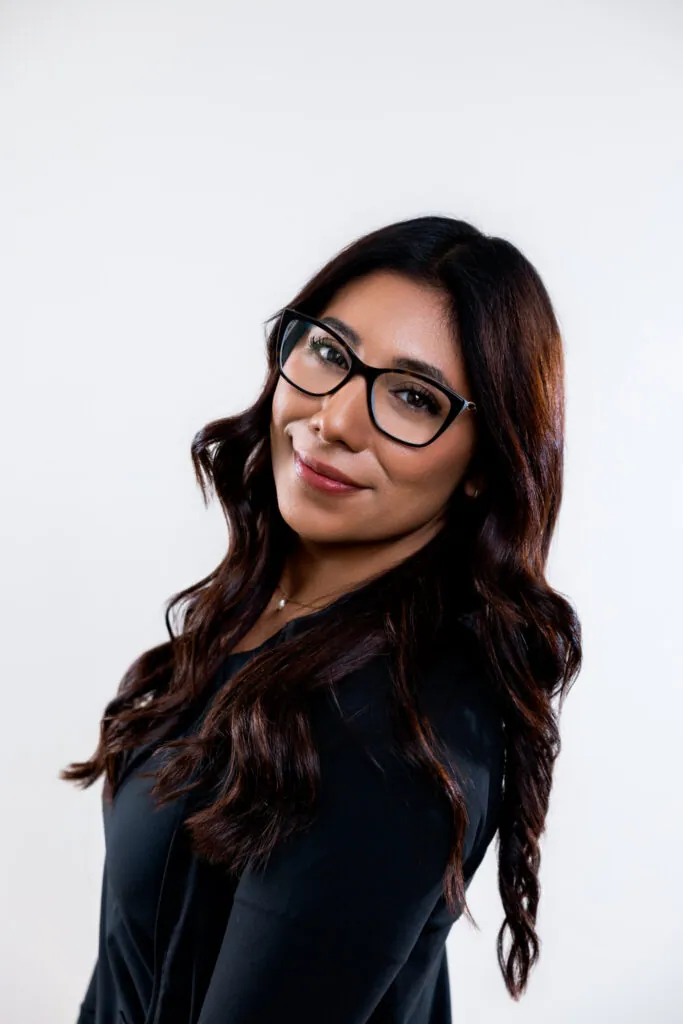 Woman with long dark wavy hair wearing black rectangular eyeglasses