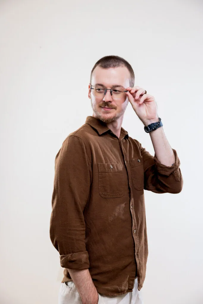 Man in a brown shirt adjusting his clear-frame eyeglasses