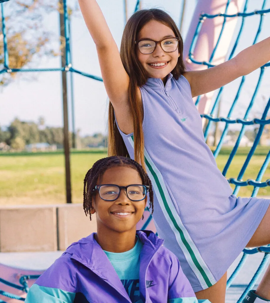 Two smiling kids wearing Nike eyeglasses on a playground