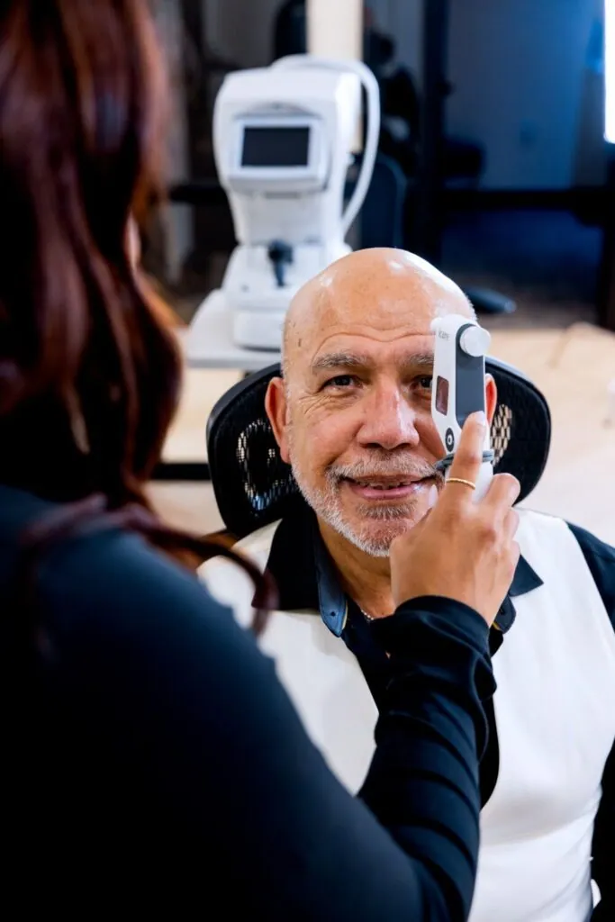 Johnny, Village Vision Center’s lab manager, smiling as a team member checks his eye pressure with a handheld tonometer