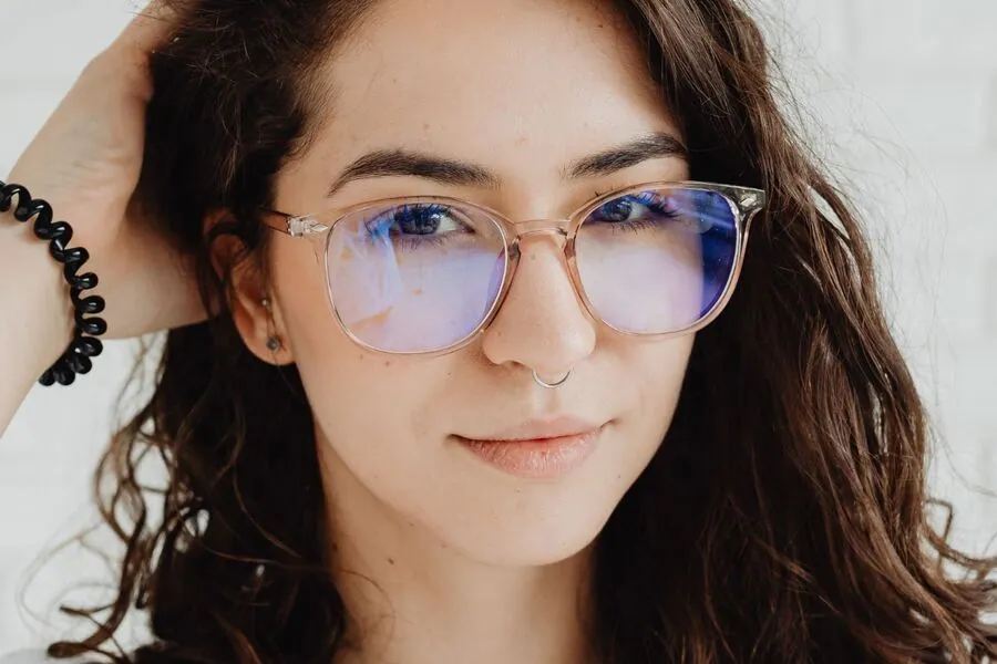 Woman wearing clear pink frames whose lenses show the faint colored reflection of a lens coating