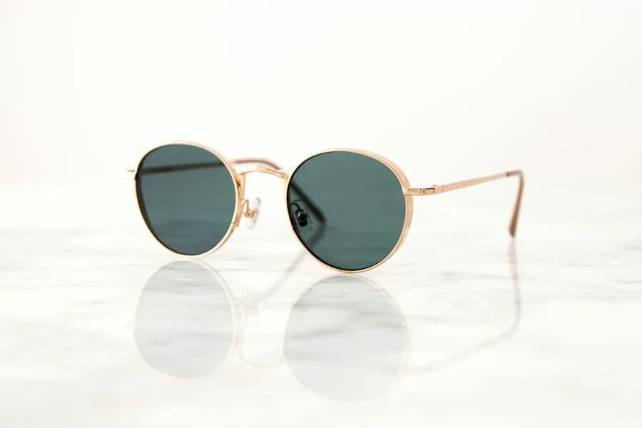 Gold round sunglasses with green lenses on a white marble surface