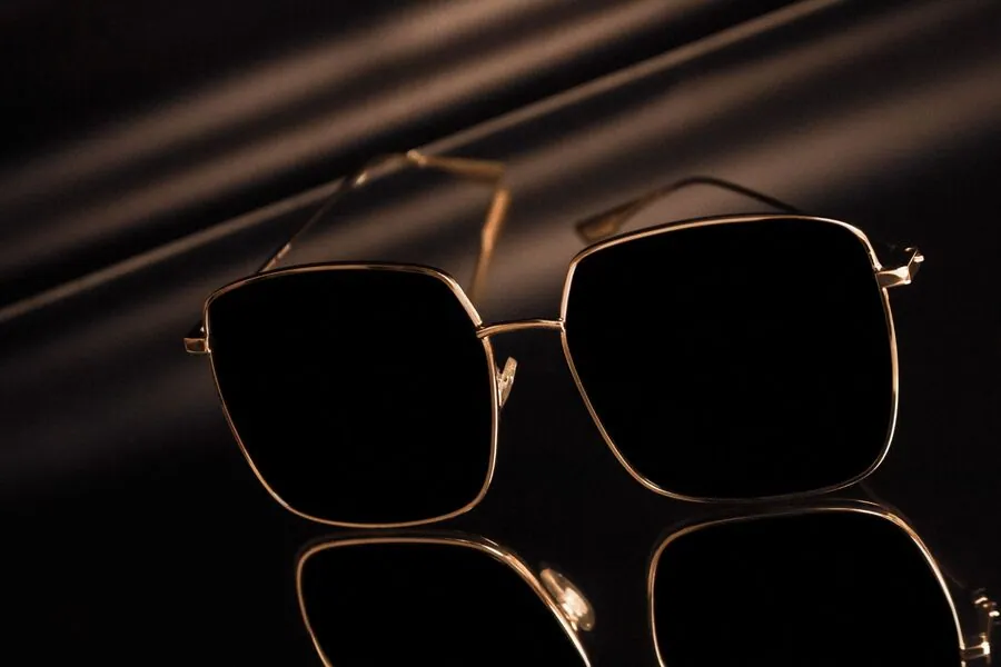 Gold square sunglasses with dark tinted lenses on a black reflective surface