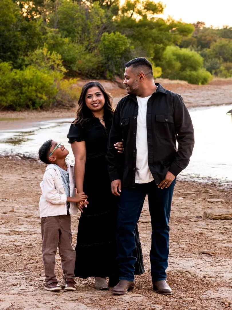 Dr. Anisha Jacob with her husband, Rony, and their son, Jagger, on the shore of a lake at sunset