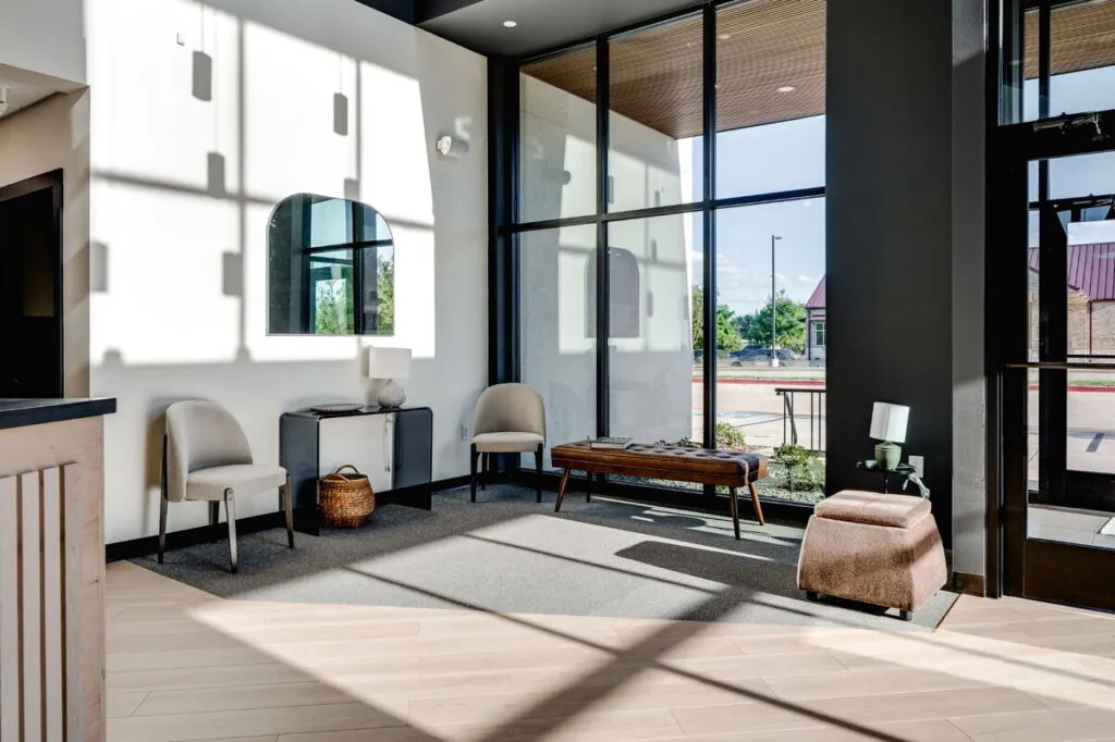 The sunlit lobby seating area at Village Vision Center, with chairs and a leather bench by tall windows