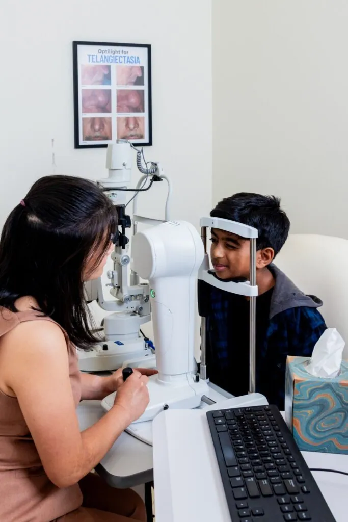 A doctor mapping a young patient's cornea with the corneal topographer as he rests his chin on the instrument